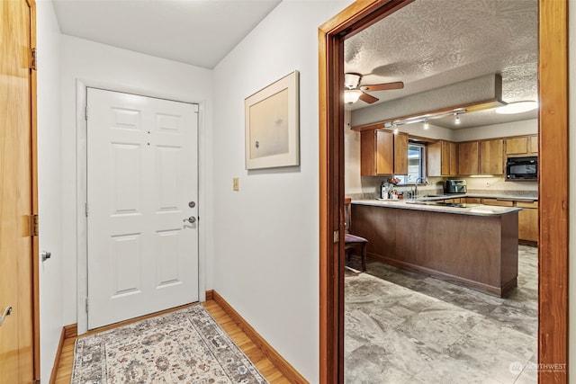 entryway featuring ceiling fan, sink, light wood-type flooring, and a textured ceiling