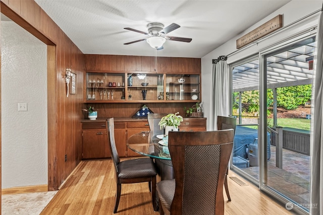 dining area with ceiling fan, light hardwood / wood-style flooring, and wooden walls