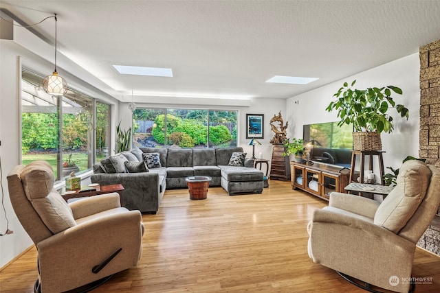 living room featuring a textured ceiling, light wood-type flooring, a skylight, and plenty of natural light