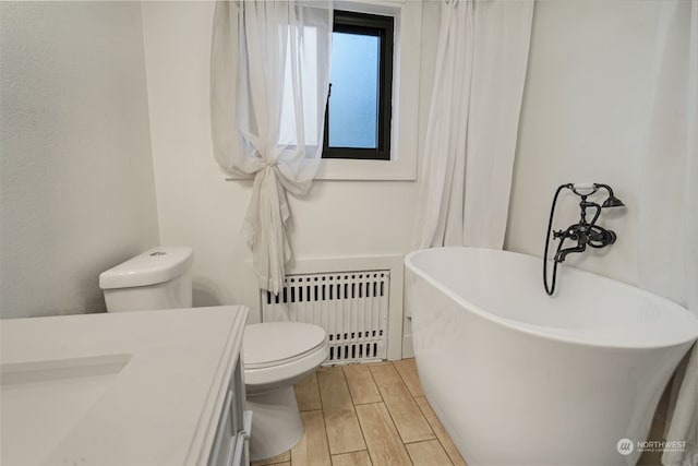 bathroom with radiator heating unit, a tub to relax in, toilet, vanity, and hardwood / wood-style flooring