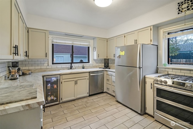 kitchen with sink, wine cooler, decorative backsplash, appliances with stainless steel finishes, and cream cabinetry