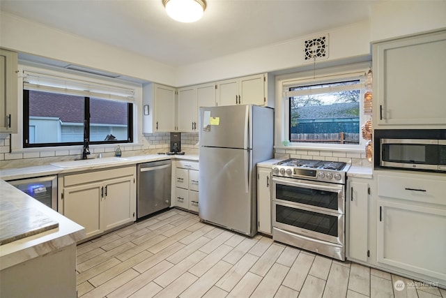 kitchen featuring sink, wine cooler, backsplash, pendant lighting, and appliances with stainless steel finishes