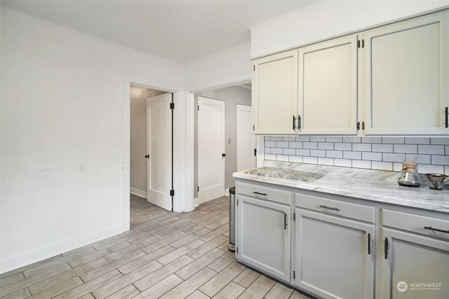 kitchen featuring backsplash, light stone countertops, crown molding, and light wood-type flooring