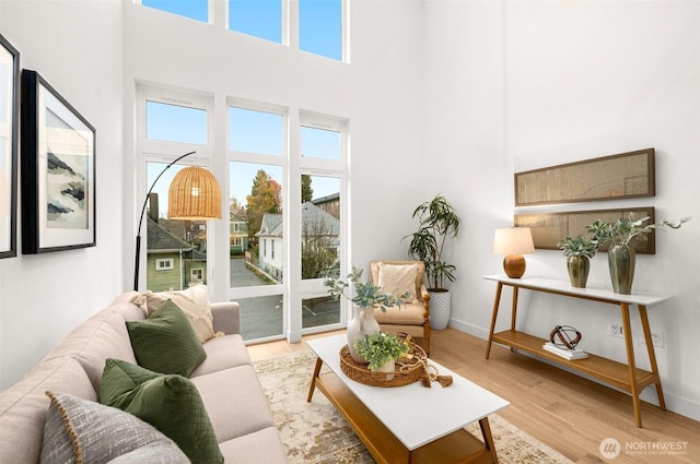 living area featuring baseboards, light wood-style floors, and a towering ceiling