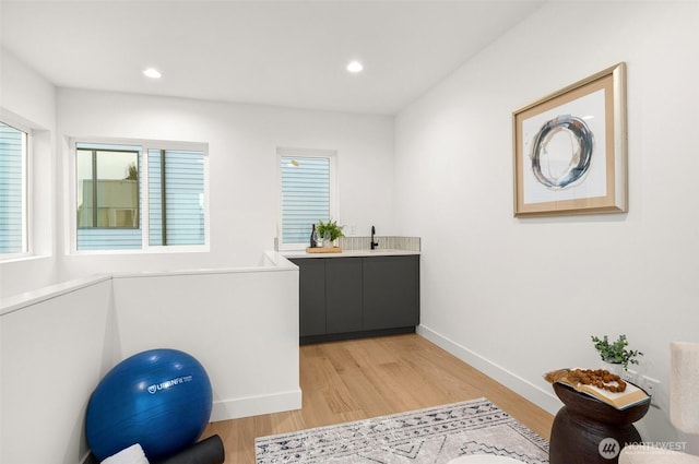 exercise area featuring recessed lighting, baseboards, light wood-style flooring, and a sink