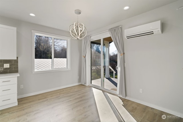 unfurnished dining area with a chandelier, a healthy amount of sunlight, light hardwood / wood-style floors, and a wall mounted air conditioner