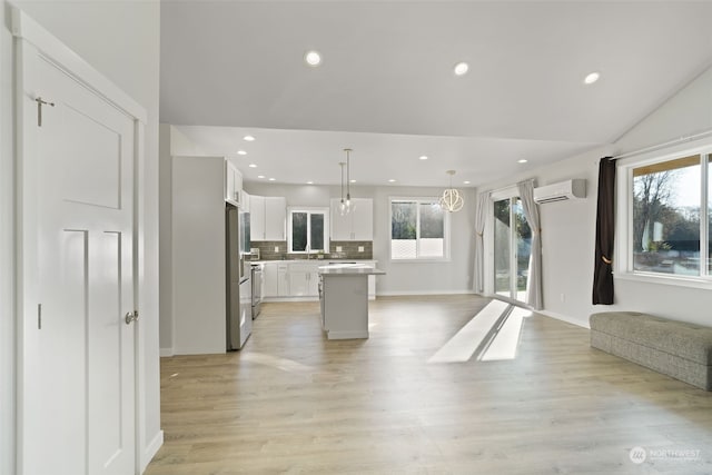 unfurnished living room featuring a wall unit AC, a healthy amount of sunlight, lofted ceiling, and light hardwood / wood-style floors