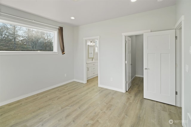 unfurnished bedroom with ensuite bath, a walk in closet, and light hardwood / wood-style flooring