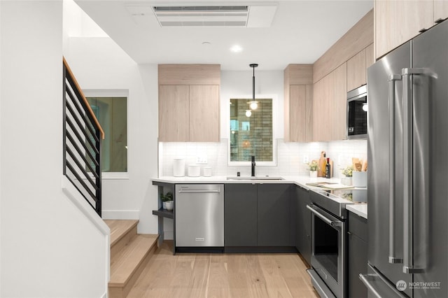 kitchen featuring sink, stainless steel appliances, decorative light fixtures, and light brown cabinets