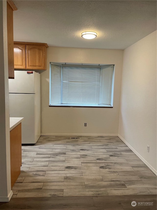 unfurnished dining area featuring light hardwood / wood-style flooring and a textured ceiling