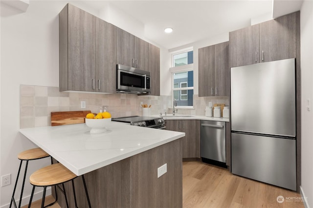 kitchen featuring kitchen peninsula, appliances with stainless steel finishes, light stone counters, a breakfast bar, and sink