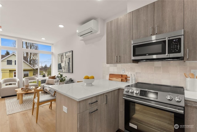 kitchen featuring stainless steel appliances, light stone counters, an AC wall unit, backsplash, and light wood-type flooring