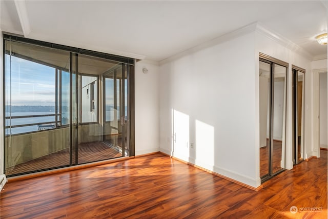 empty room with hardwood / wood-style floors, a water view, and crown molding