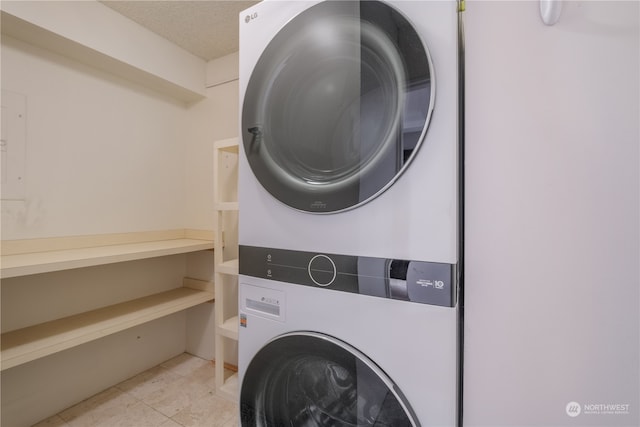 laundry area with a textured ceiling, light tile patterned floors, and stacked washer / dryer