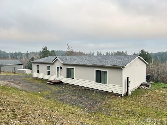 back of house with a shingled roof, a lawn, and fence