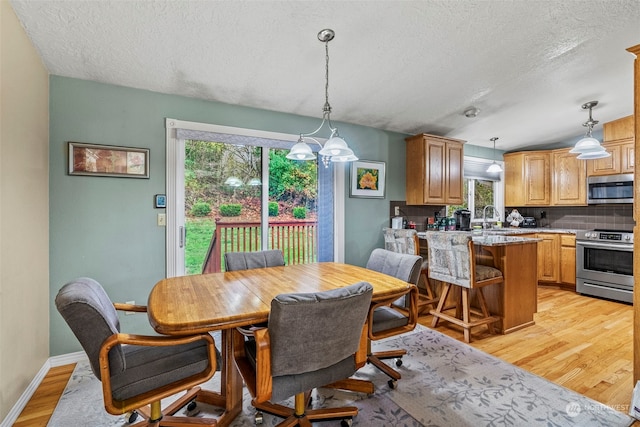 dining room featuring light wood-type flooring, a textured ceiling, vaulted ceiling, and sink