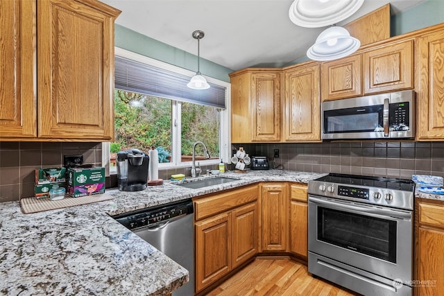 kitchen featuring decorative backsplash, light stone countertops, stainless steel appliances, sink, and light hardwood / wood-style floors