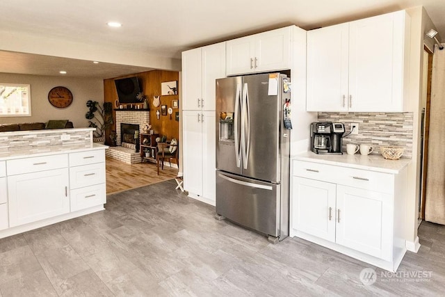 kitchen with a brick fireplace, stainless steel fridge with ice dispenser, decorative backsplash, light hardwood / wood-style flooring, and white cabinetry