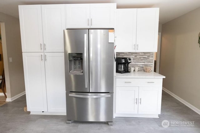 kitchen with stainless steel fridge with ice dispenser, white cabinetry, and light stone counters