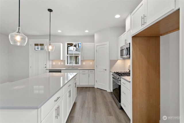 kitchen with decorative light fixtures, a center island, sink, appliances with stainless steel finishes, and white cabinets