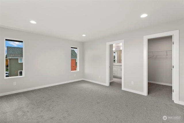 unfurnished bedroom with ensuite bathroom, a closet, a spacious closet, and light carpet