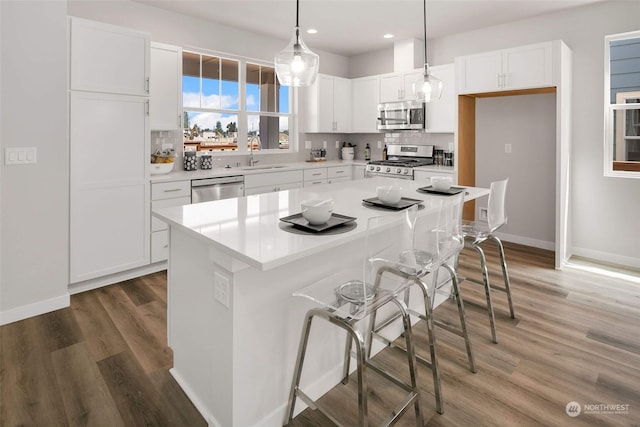 kitchen featuring hanging light fixtures, stainless steel appliances, white cabinetry, and a kitchen island