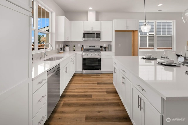 kitchen with white cabinets, dark hardwood / wood-style flooring, stainless steel appliances, sink, and hanging light fixtures