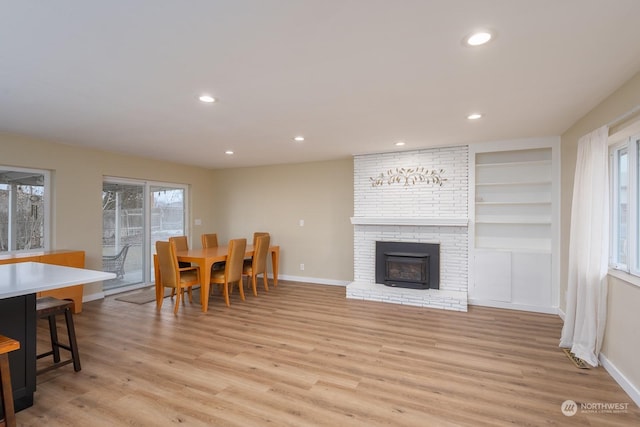 living room with built in shelves, a fireplace, and light hardwood / wood-style flooring