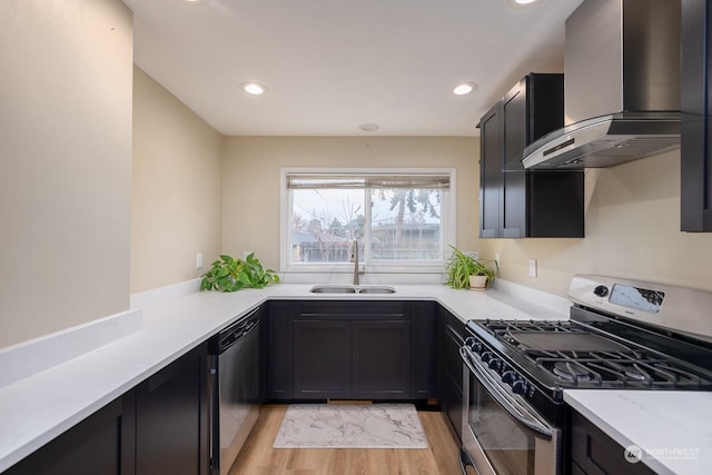 kitchen with light stone countertops, sink, wall chimney exhaust hood, light hardwood / wood-style floors, and appliances with stainless steel finishes