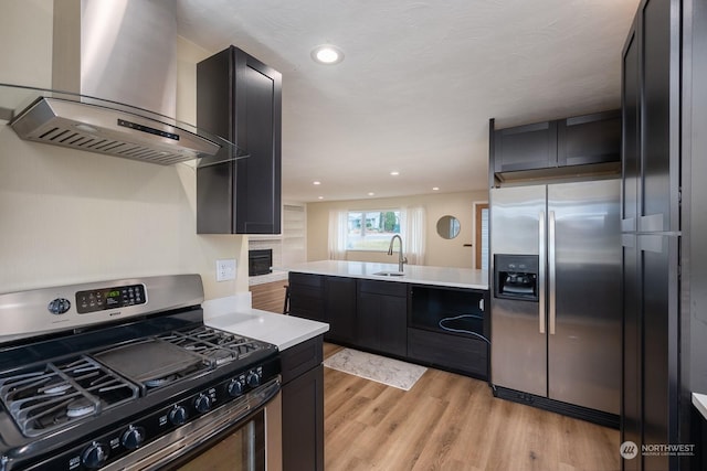 kitchen with appliances with stainless steel finishes, light hardwood / wood-style flooring, wall chimney exhaust hood, and sink