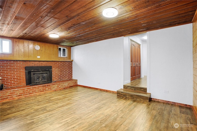 unfurnished living room featuring a wood stove, wooden walls, wood ceiling, and light wood-type flooring