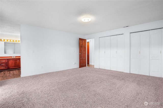 unfurnished bedroom with connected bathroom, carpet floors, two closets, and a textured ceiling