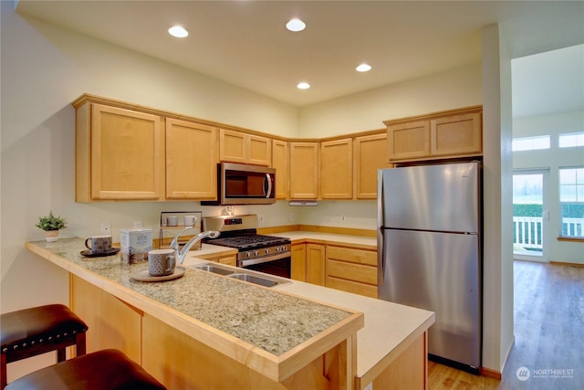 kitchen with light brown cabinets, sink, light wood-type flooring, kitchen peninsula, and stainless steel appliances