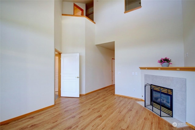 unfurnished living room featuring a tile fireplace, a towering ceiling, and light hardwood / wood-style floors