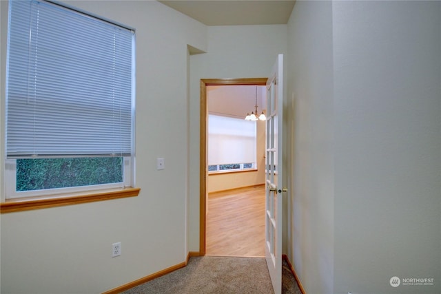 hallway with light colored carpet and a notable chandelier