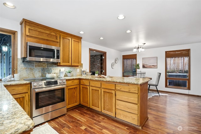 kitchen featuring dark wood-type flooring, stainless steel appliances, decorative backsplash, kitchen peninsula, and a chandelier