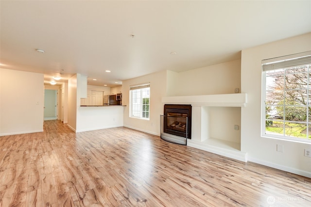 unfurnished living room with light wood finished floors, a glass covered fireplace, and baseboards