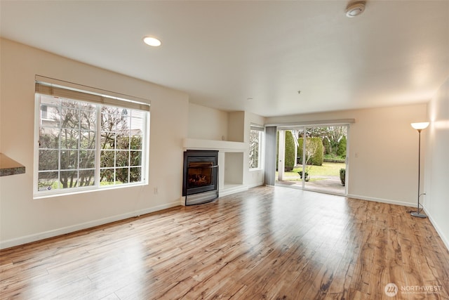 unfurnished living room featuring light wood finished floors, recessed lighting, a glass covered fireplace, and baseboards