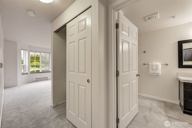 hall with a baseboard heating unit, light carpet, and baseboards