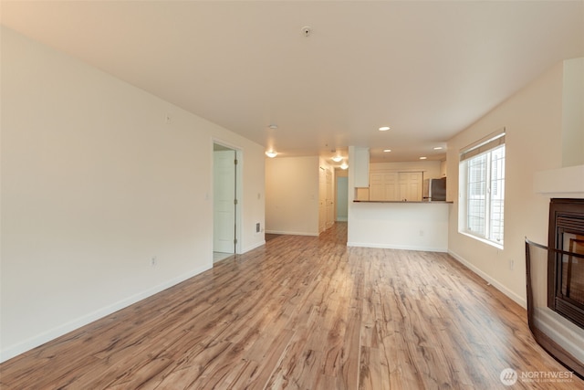 unfurnished living room with light wood-type flooring, a glass covered fireplace, baseboards, and recessed lighting