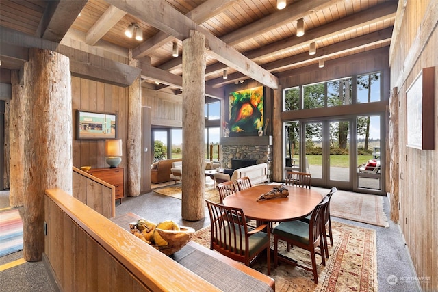 dining space with beam ceiling, a stone fireplace, and wooden walls