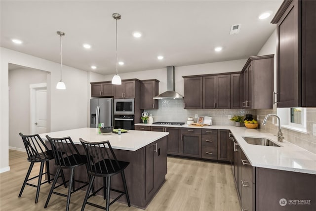 kitchen with stainless steel appliances, sink, wall chimney range hood, decorative light fixtures, and a kitchen island