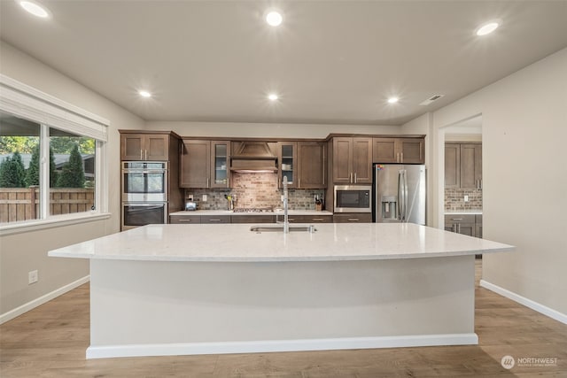 kitchen with a large island with sink, stainless steel appliances, and light hardwood / wood-style floors