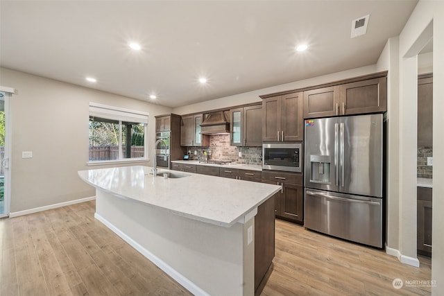 kitchen with stainless steel appliances, light hardwood / wood-style floors, and an island with sink