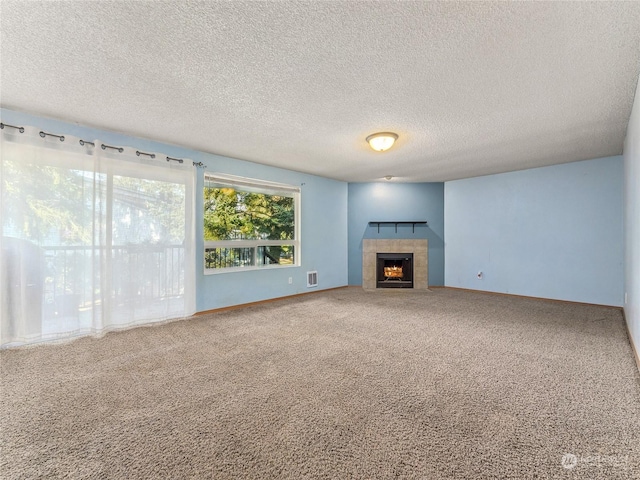 unfurnished living room featuring carpet flooring, a tile fireplace, and a textured ceiling