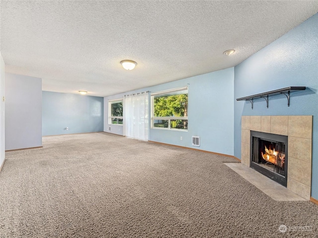 unfurnished living room with a tiled fireplace, light carpet, and a textured ceiling