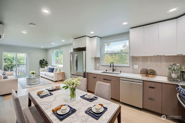 kitchen featuring appliances with stainless steel finishes, a healthy amount of sunlight, sink, light hardwood / wood-style flooring, and white cabinets