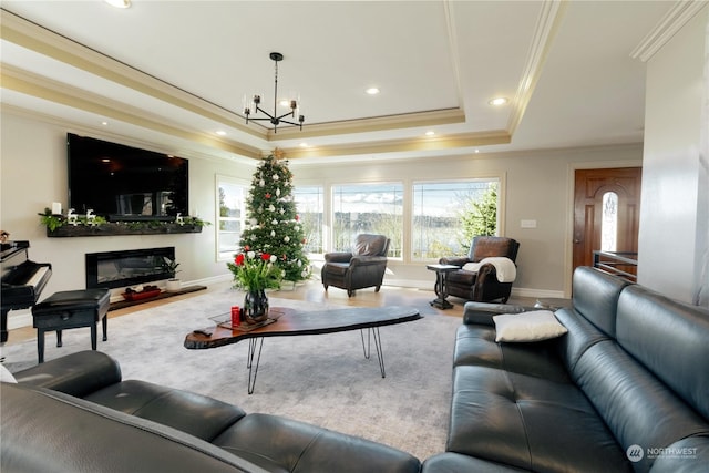 living area featuring a glass covered fireplace, an inviting chandelier, a tray ceiling, crown molding, and recessed lighting