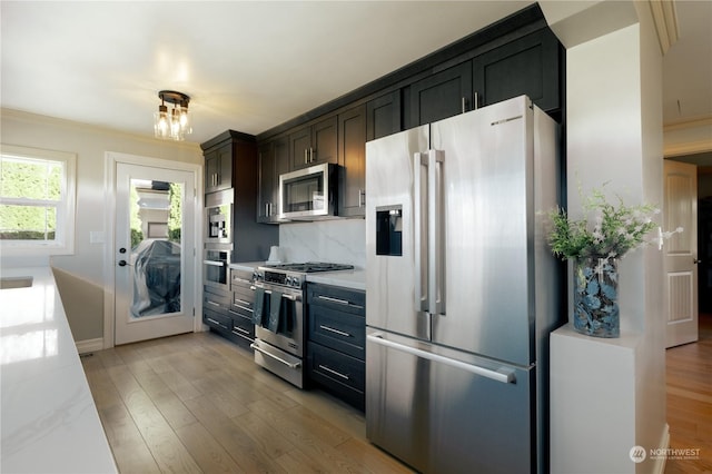 kitchen featuring light wood finished floors, appliances with stainless steel finishes, light stone counters, and backsplash