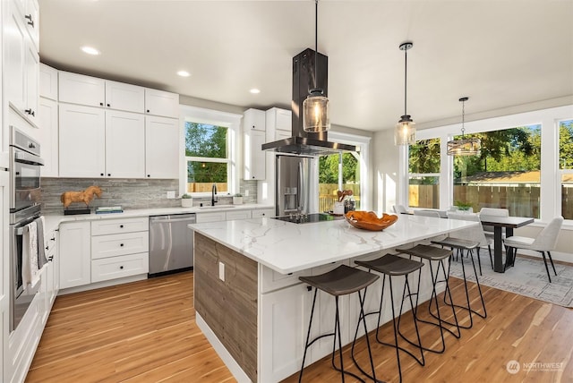 kitchen featuring white cabinetry, a center island, island range hood, and appliances with stainless steel finishes